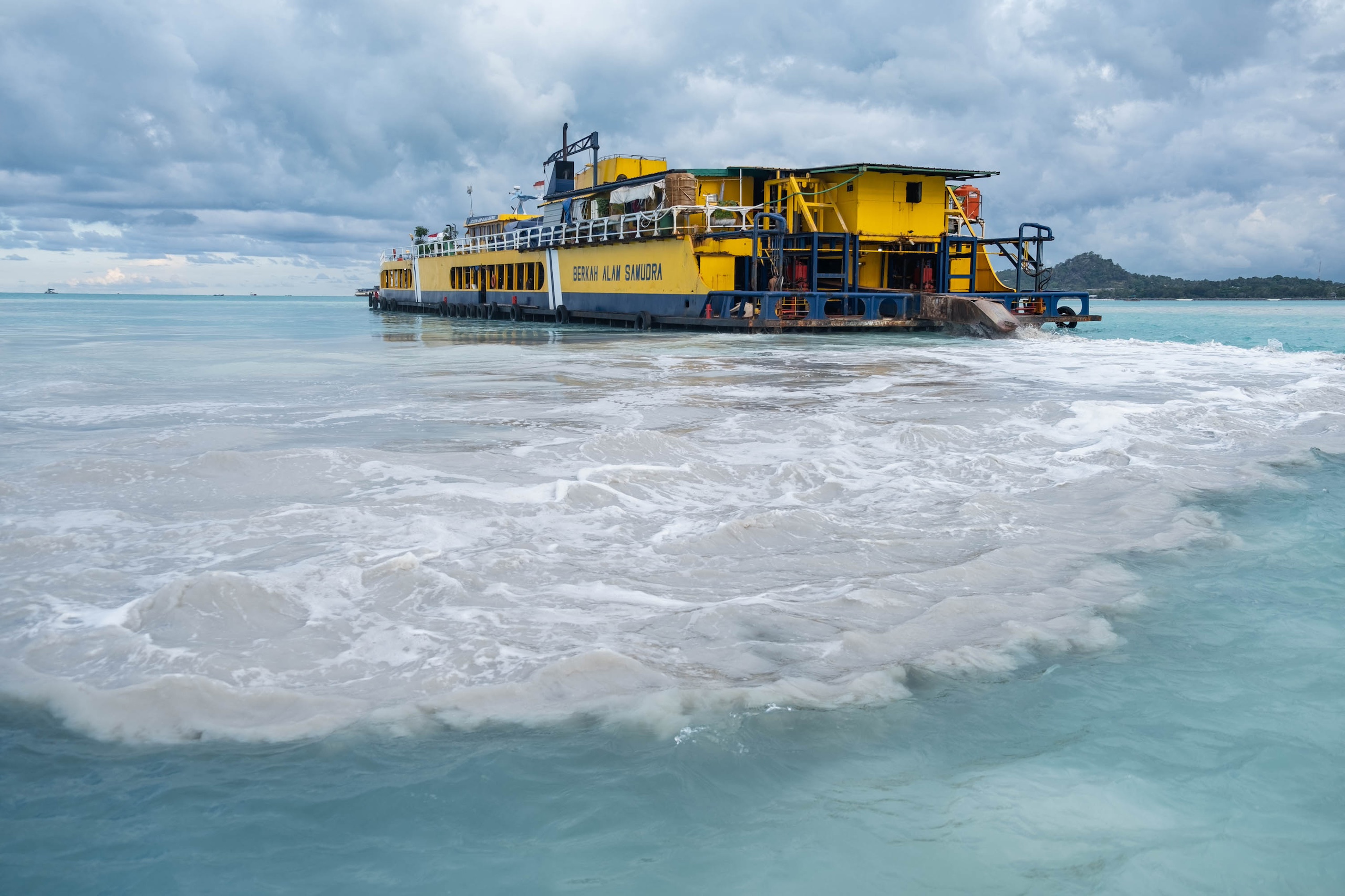 A large yellow mining pontoon releases grey sediment into turquoise seawater.