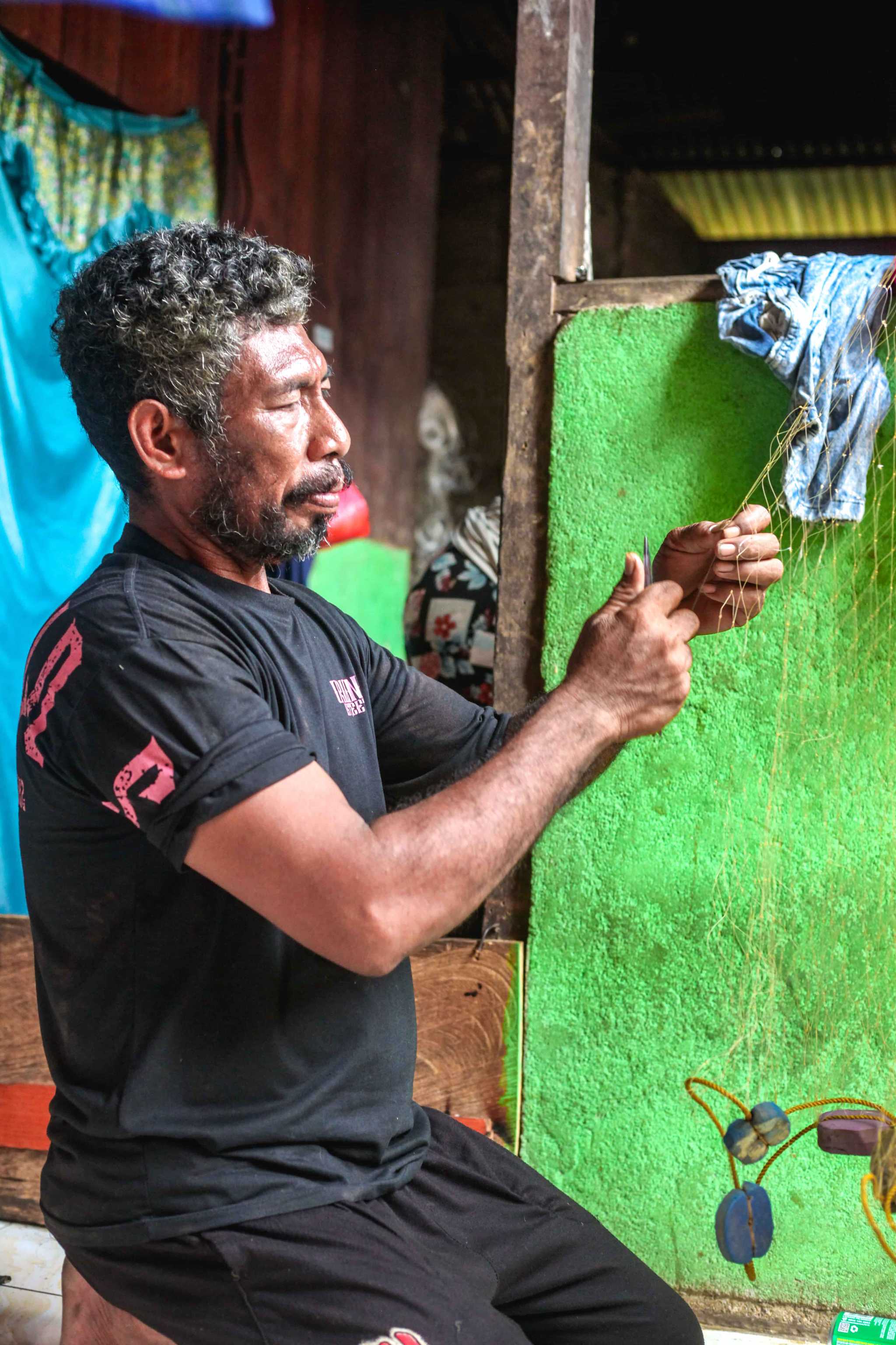 Fisherman sits and fixes a fishing net