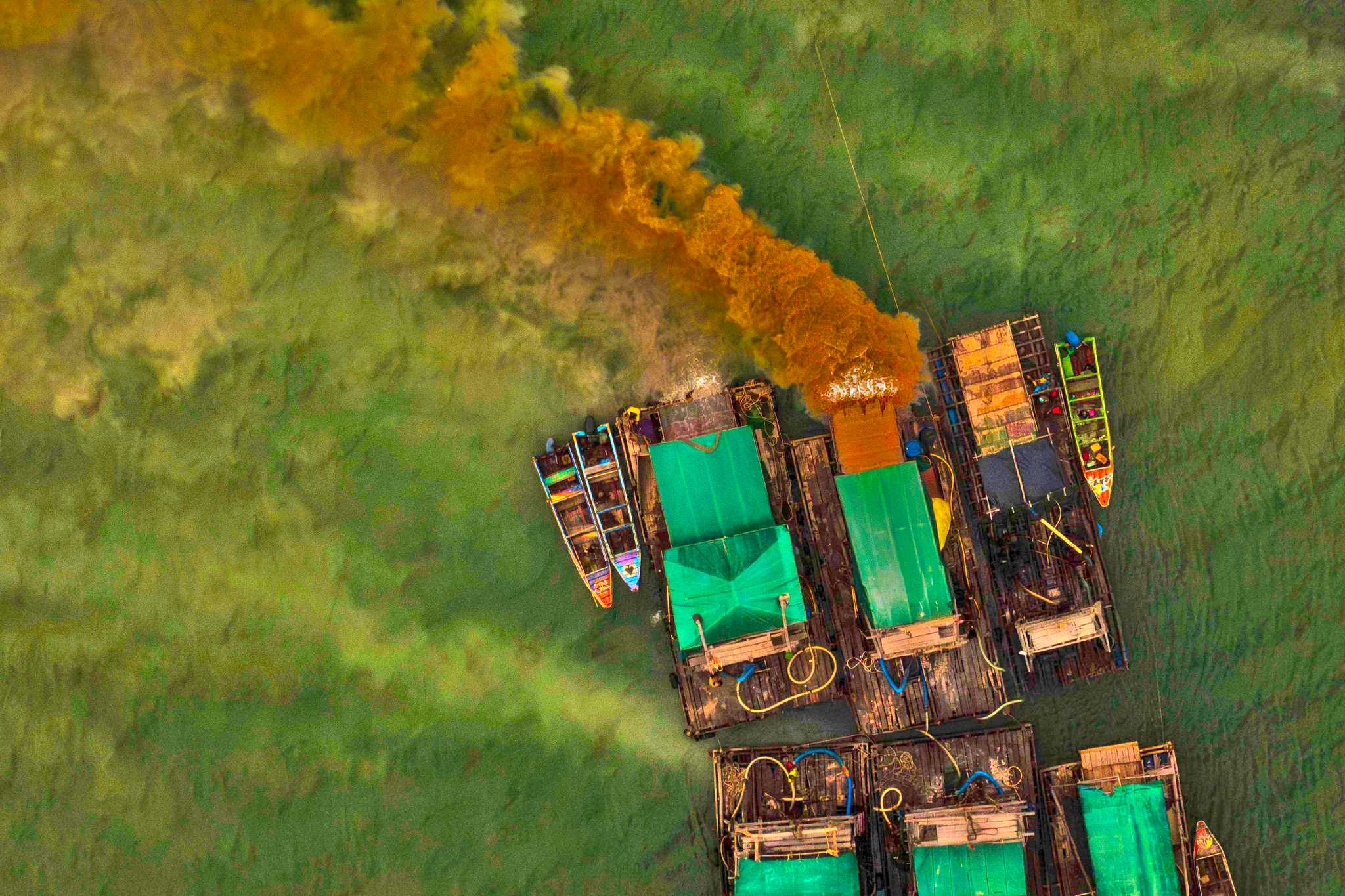 Drone view of green wooden boats discharging brown sediment into seawater